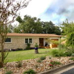 This is another view of the house from the left side. You can see closer views of the river rock beds with multi-colored lantana, native grasses, and an eight foot Crepe Myrtle Tree with red blossoms.