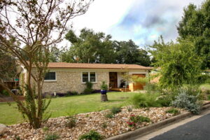 This is another view of the house from the left side. You can see closer views of the river rock beds with multi-colored lantana, native grasses, and an eight foot Crepe Myrtle Tree with red blossoms.