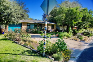 Front view of house and flower beds with a yield sign that a friendly neighbor has woven bright colored stripes of yarn around the pole.