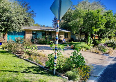 Front view of house and flower beds with a yield sign that a friendly neighbor has woven bright colored stripes of yarn around the pole.