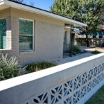 This image displays a close-up view of the Mid-Century breeze blocks and concrete half wall. Behind the wall you can see a bed made of small white limestone pebbles with an evergreen trailing plant and a dwarf silver cloud sage bush.