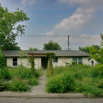 This image is a front View of the June 2023 Yard of the Month located at 1414 Ridgemont Dr. Described as a pocket Prairie, you are greeted with a wood pergola over the walkway. It is surrounded by colorful Texas natives and Pollinators. The house has a stone pathway which leads you to the front door and curves around several flower beds.
