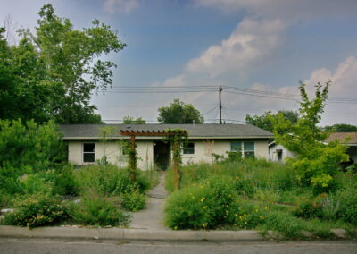 This image is a front View of the June 2023 Yard of the Month located at 1414 Ridgemont Dr. Described as a pocket Prairie, you are greeted with a wood pergola over the walkway. It is surrounded by colorful Texas natives and Pollinators. The house has a stone pathway which leads you to the front door and curves around several flower beds.