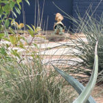 A little garden gnome framed by grasses and coral yuccas.