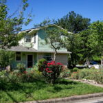 This image depicts the front of the May 2023 yard of the month located at 1501 Corona. It shows various beds of red poppies, painted daisies, and red knockout roses.