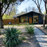 A front view of 1419 Westmoor Dr. with a limestone walkway leading to the Navy painted home with a bright orange door. Along the walkway you'll find decomposed granite beds with yuccas and agaves.