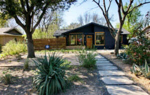 A front view of 1419 Westmoor Dr. with a limestone walkway leading to the Navy painted home with a bright orange door. Along the walkway you'll find decomposed granite beds with yuccas and agaves.