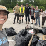 Eight volunteers for the Tannahill Branch cleanup posing in front of the trash that they had removed from the creek including a bicycle frame and about 13 bags of trash.