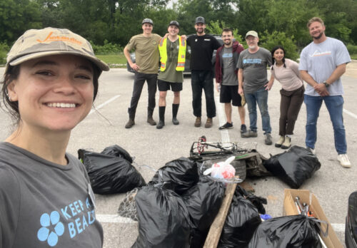 Eight volunteers for the Tannahill Branch cleanup posing in front of the trash that they had removed from the creek including a bicycle frame and about 13 bags of trash.
