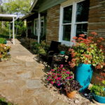 View of a stone pathway lined with turquoise colored flower pots and orange and pink flowers.