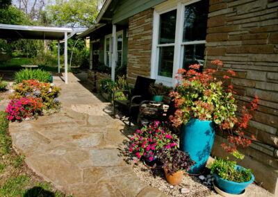 View of a stone pathway lined with turquoise colored flower pots and orange and pink flowers.