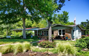 A street view of the house depicting two oak trees surrounded by rock lined beds with native grasses and red salvia greggi.