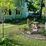A side view of the house with a rock lined flower bed where you'll find a bird bath and red knockout roses.