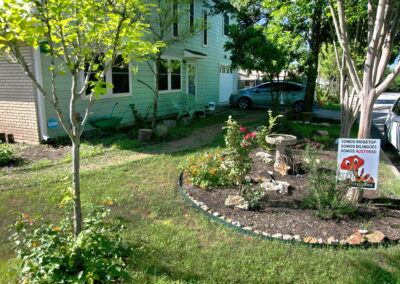 A side view of the house with a rock lined flower bed where you'll find a bird bath and red knockout roses.