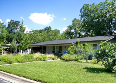 A left side curb view of 1802 Corona Dr. The image displays a medium size Fig Tree in the middle of a yard of grass as well as a small Desert Willow.