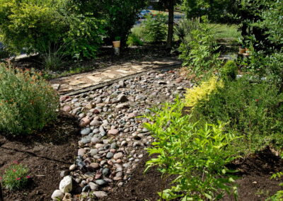 A side bed filled with various colors of river rock. There is also a yellow bell, orange salvia greggi, coral yucca, and a sweet william.