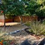 Another view of the right of driveway. You see beds lined with medium sized limestone rocks and filled with river rock. You'll also find two small oak trees and a light green sage bush.