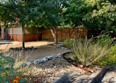 Another view of the right of driveway. You see beds lined with medium sized limestone rocks and filled with river rock. You'll also find two small oak trees and a light green sage bush.