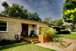 Another view of the front porch which has been extended as a deck. The deck has two lounge chairs on each side of the front door. Potted plants are also displayed.