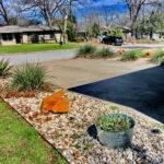 A view from the top of the driveway looking towards the street. You'll find the driveway lined with white rock beds containing beautiful large brown rocks and coral yuccas and cacti.