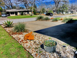 A view from the top of the driveway looking towards the street. You'll find the driveway lined with white rock beds containing beautiful large brown rocks and coral yuccas and cacti.