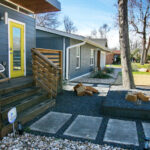 A close up view of the front tiered beds of the guest house which are filled with small dark grey gravel and are lined with steel. The beds also contain large brown and tan rocks and they are adjacent to the concrete paver walkway.