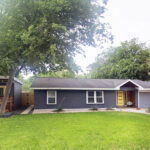 A front distant front view of the entire property where you'll find the main house and guest house to the left. The image also depicts the large area of green grass and a large pecan tree.