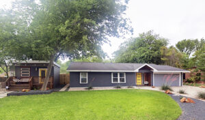 A front distant front view of the entire property where you'll find the main house and guest house to the left. The image also depicts the large area of green grass and a large pecan tree.