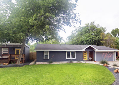 A front distant front view of the entire property where you'll find the main house and guest house to the left. The image also depicts the large area of green grass and a large pecan tree.