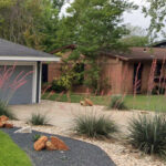 This a view of the drive way which is lined with curved beds of white rock and includes several blooming coral yuccas. The yuccas bloom tall arching stalks with coral flowers which attract hummingbirds.